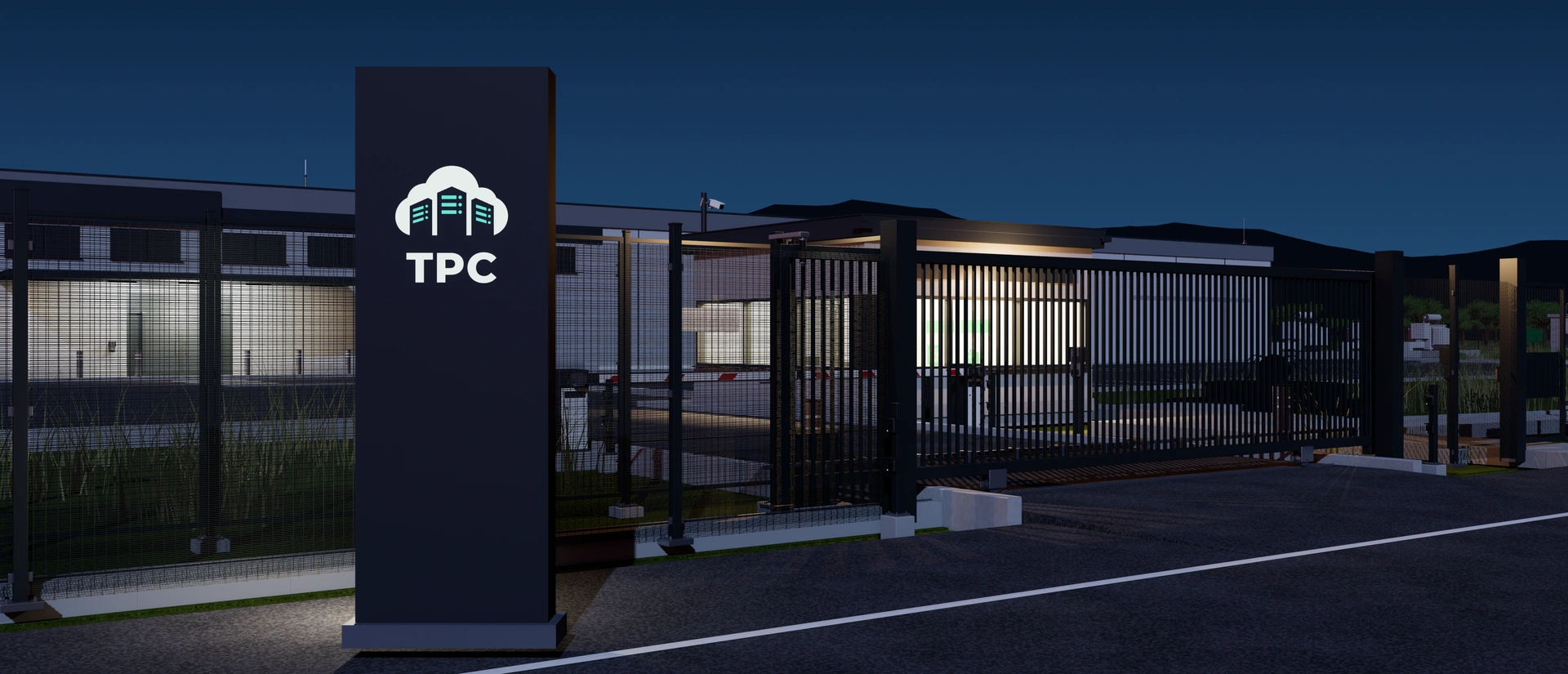 The entrance to the TPC campus at dusk: the TPC sign, the perimeter fence and the closed vehicle gate, with the lit gatehouse behind